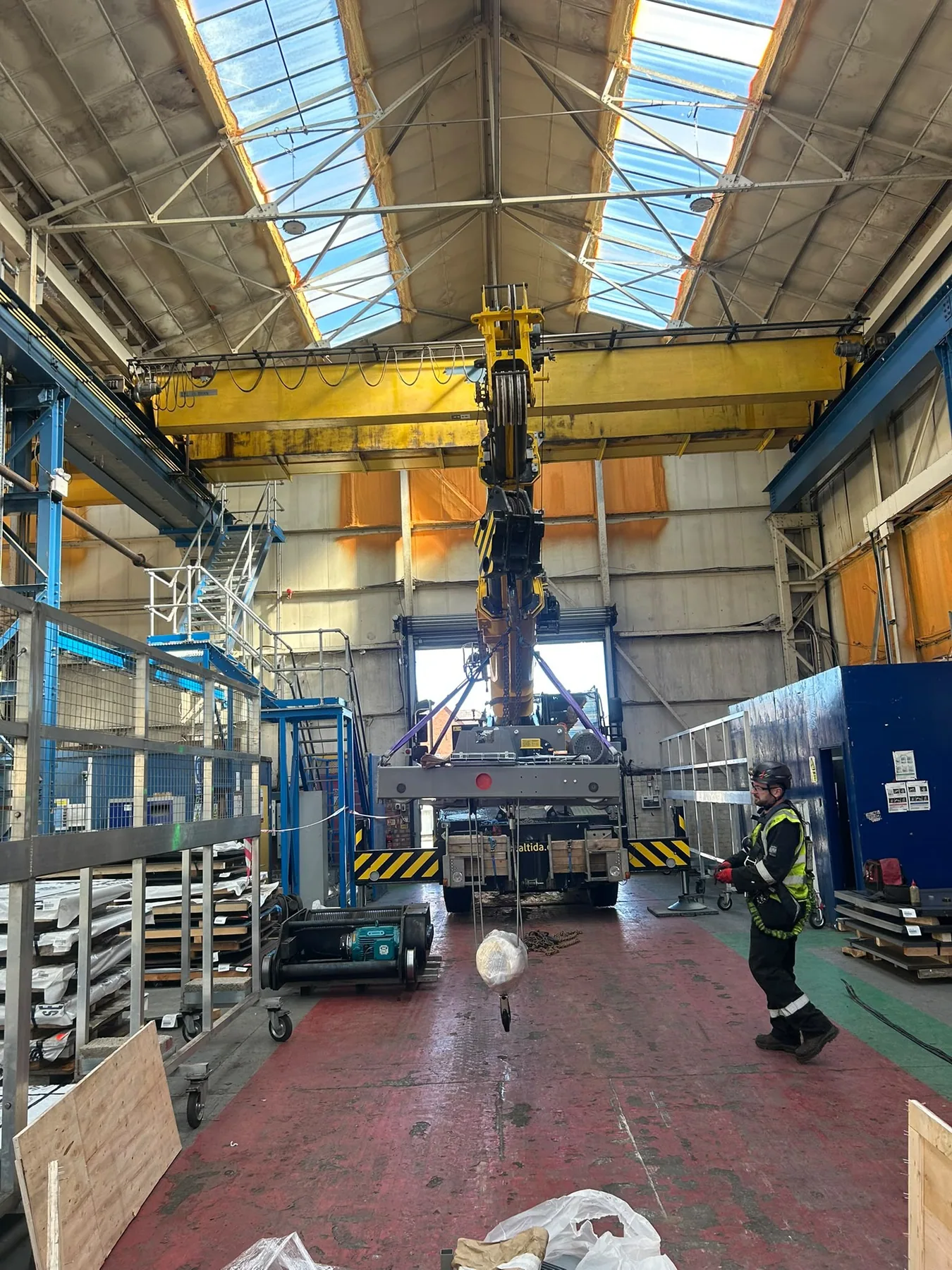 Engineer operating an overhead crane with lifting equipment suspended in a factory workshop